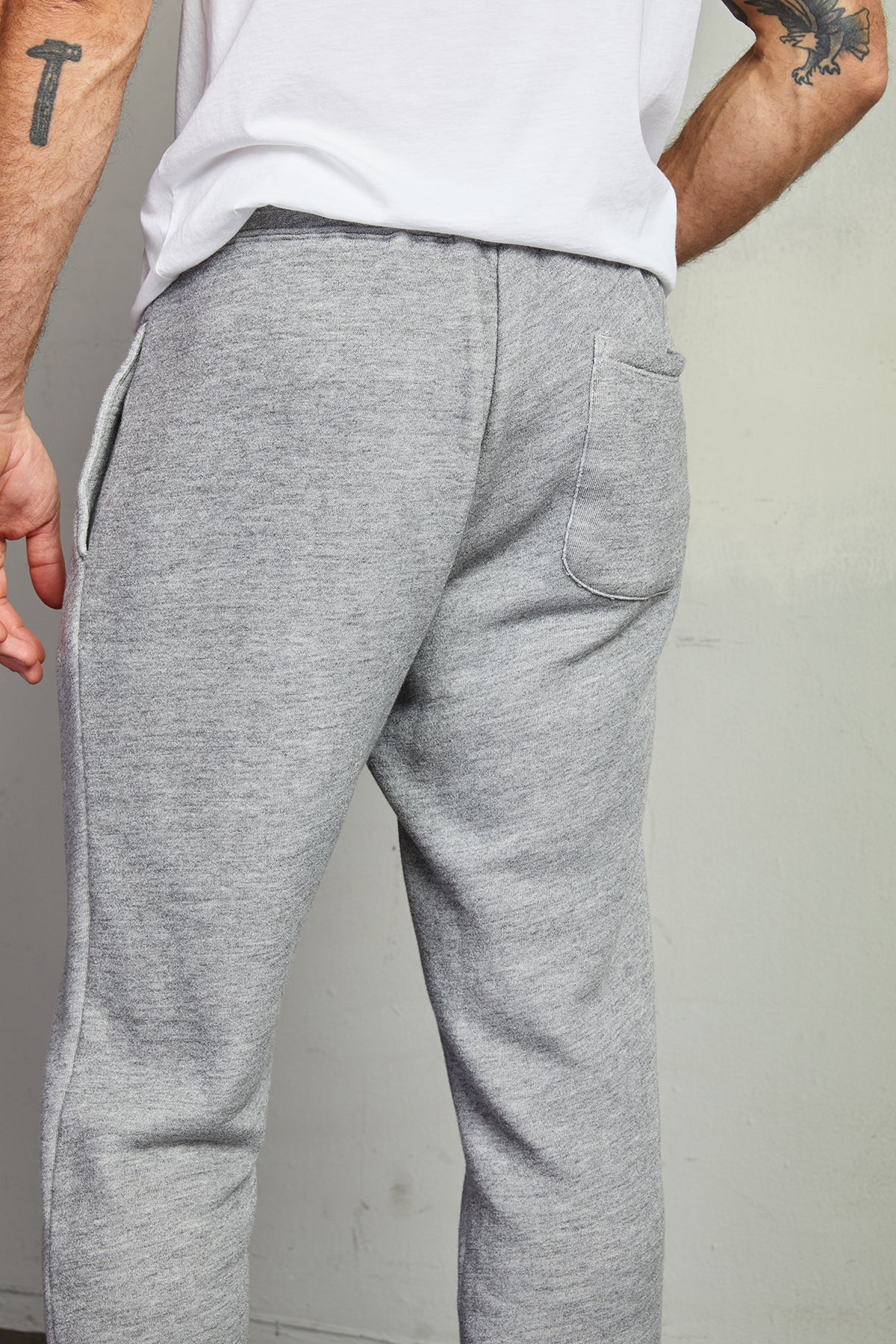 A person in a white shirt and HUGH FLEECE JOGGER sweatpants in heathered grey by Velvet by Graham & Spencer is seen from the back, showcasing tattoos on their arm.-7990567993425