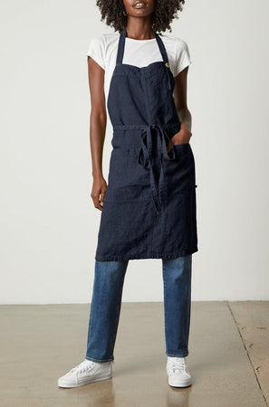 A woman wearing a navy LINEN APRON from Jenny Graham Home and jeans with an adjustable neck strap.