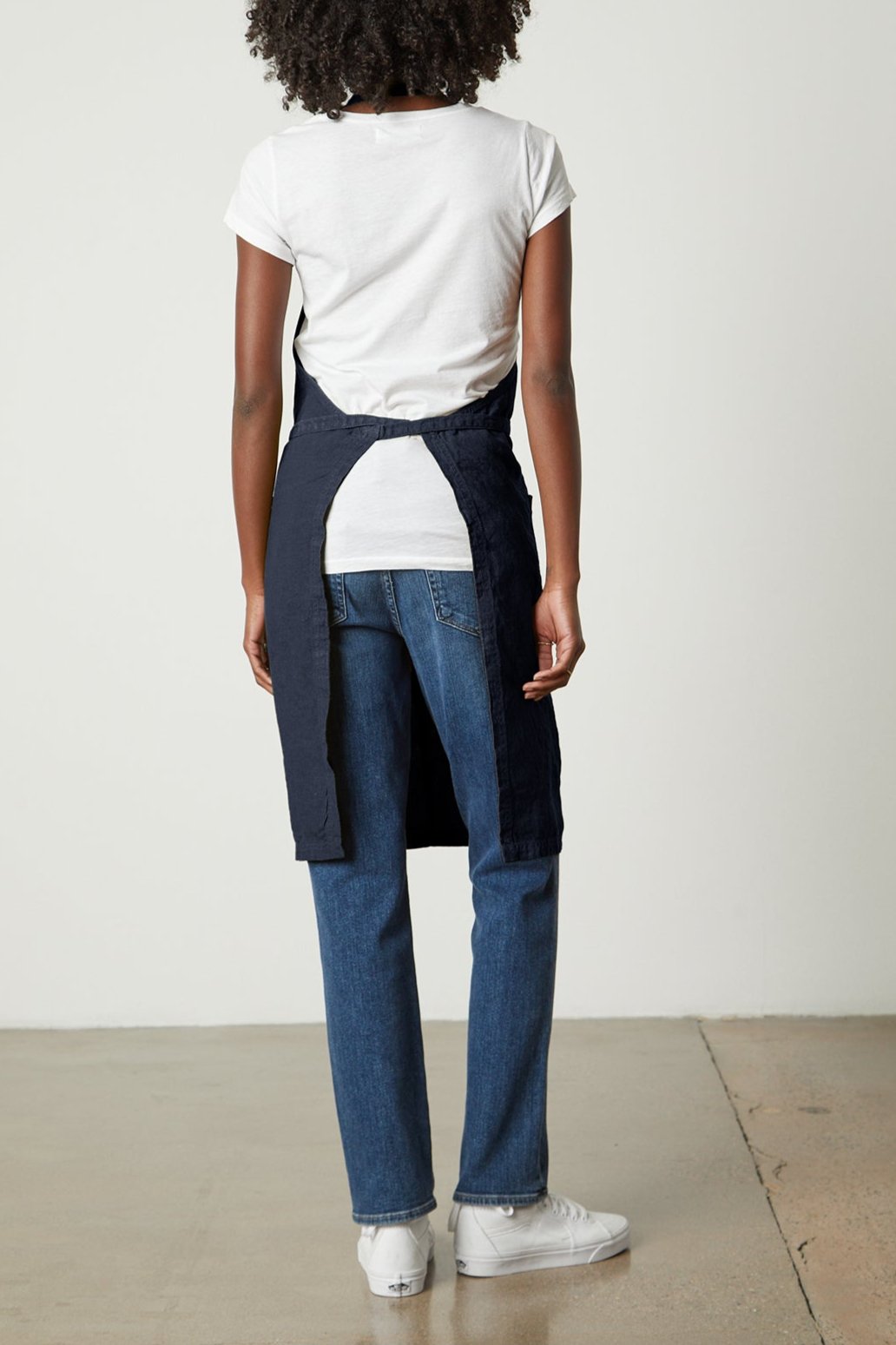 The back view of a woman wearing Jenny Graham Home durable linen jeans and an adjustable neck strap LINEN APRON.-25519629500609