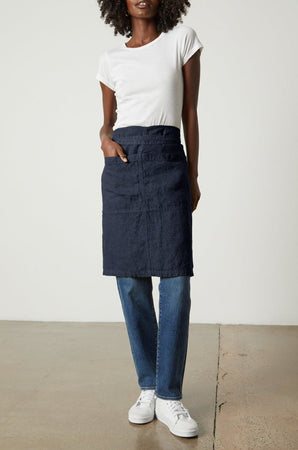 A woman wearing a durable Jenny Graham Home linen apron, unisex apron with an adjustable neck strap and white t-shirt.