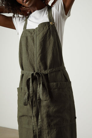 Person wearing a white t-shirt and a green Jenny Graham Home LINEN APRON with large pockets adjusts the adjustable neck strap.