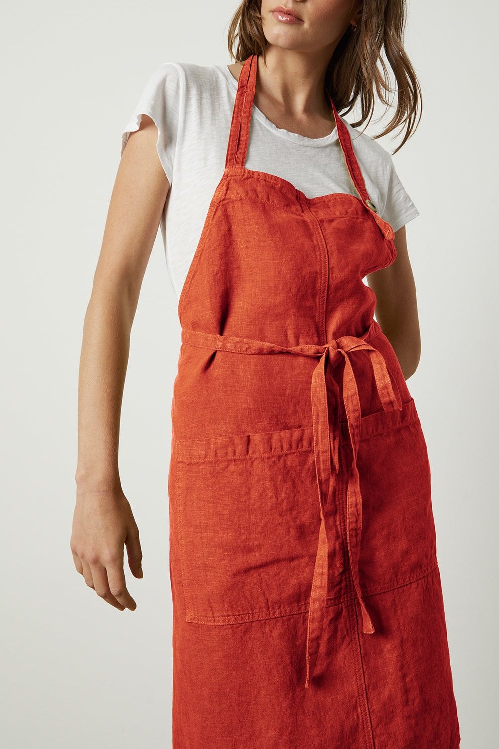 A woman wearing a white shirt and a red Jenny Graham Home LINEN APRON with an adjustable neck strap stands against a plain background.-25519629959361