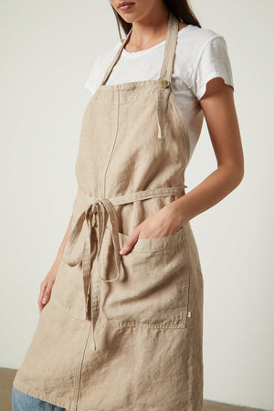 A person wearing a durable Jenny Graham Home LINEN APRON over a white shirt, with hands tucked into the adjustable neck strap pockets.