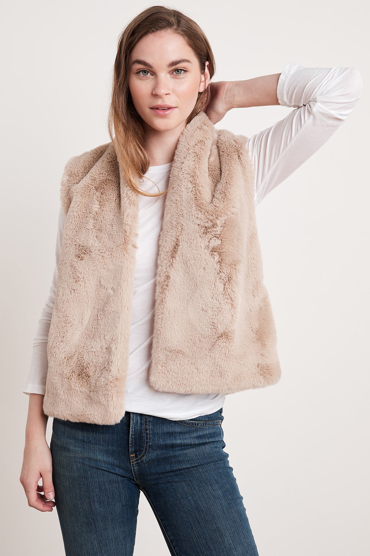 A woman in a white long-sleeve shirt and blue jeans poses while wearing the CHELLE FAUX LUX FUR OPEN VEST by Velvet by Graham & Spencer, an eco-chic piece perfect for layering during the cooler months.-5697530167377