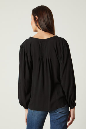 the back view of a woman wearing jeans and an EMILY V-NECK BLOUSE by Velvet by Graham & Spencer.