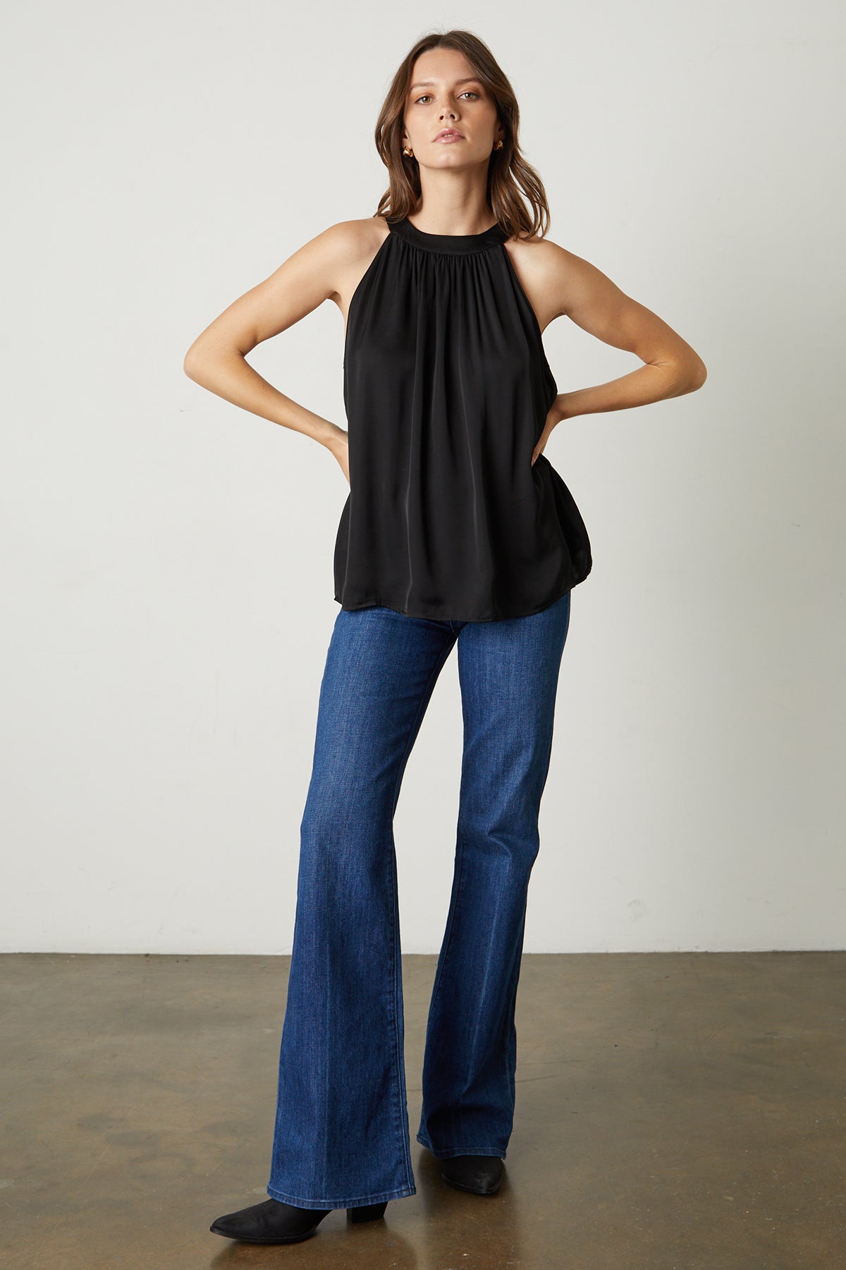 Model standing with hands on hips wearing Crystal Satin Halter Top in black with blue denim and black boots full length front