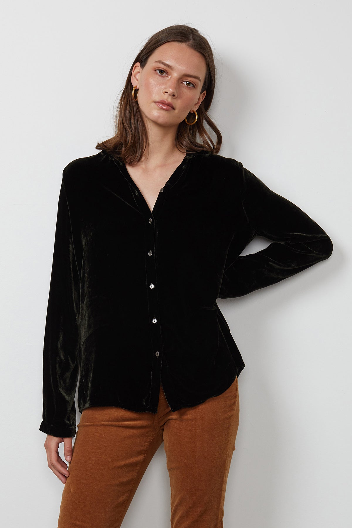 A person with shoulder-length hair wearing a JENSINE Silk Velvet Button-Up Shirt by Velvet by Graham & Spencer and brown pants stands against a plain white background.-15201374568641