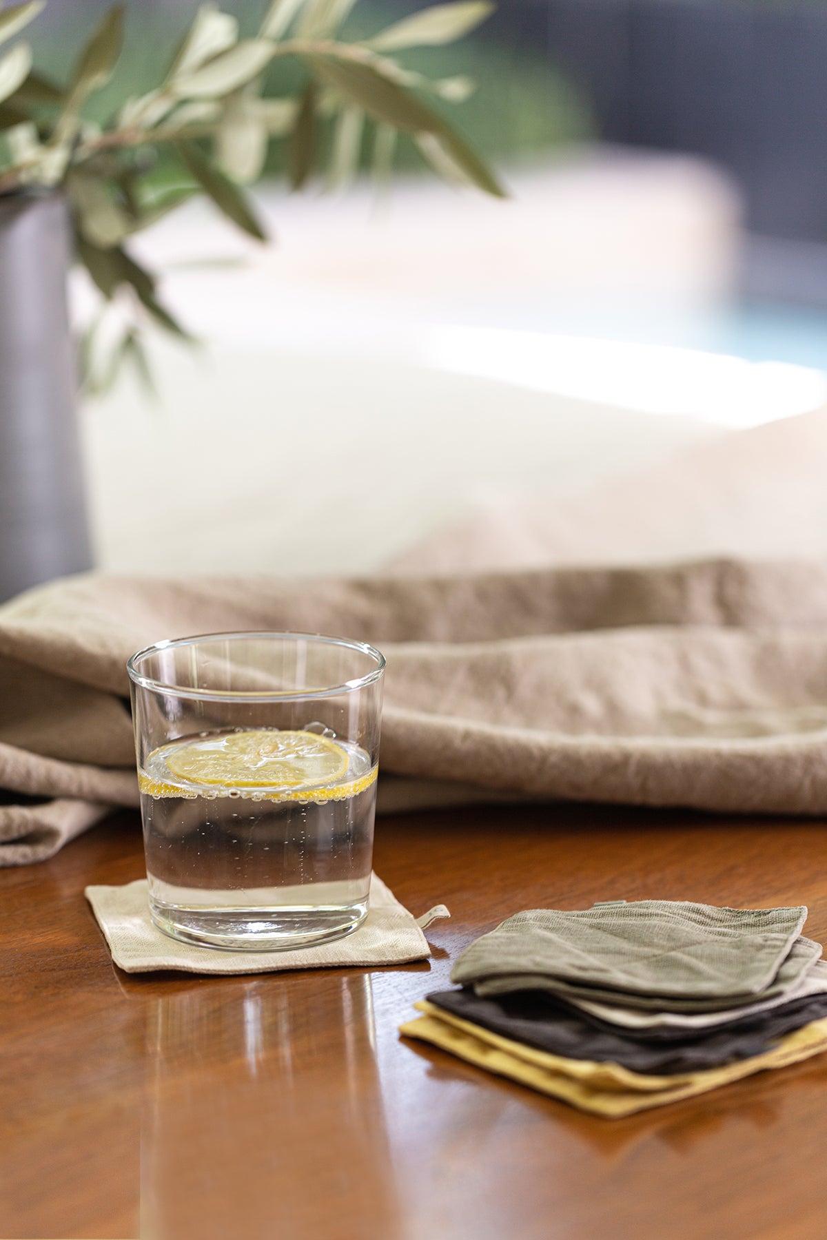 a set of 4 Linen Coasters by Jenny Graham Home on a table next to a plant.-14899252330689