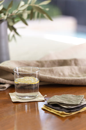 a set of 4 Linen Coasters by Jenny Graham Home on a table next to a plant.