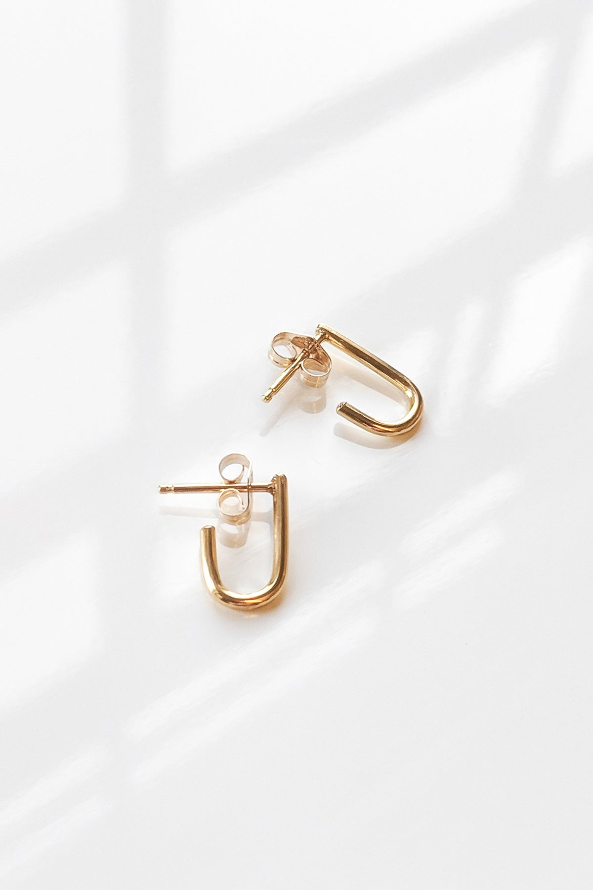 The SELMA GOLD EARRINGS BY THATCH from Thatch, featuring a modern curved design in gold vermeil, are displayed on a white surface with soft shadows.-5730759147601