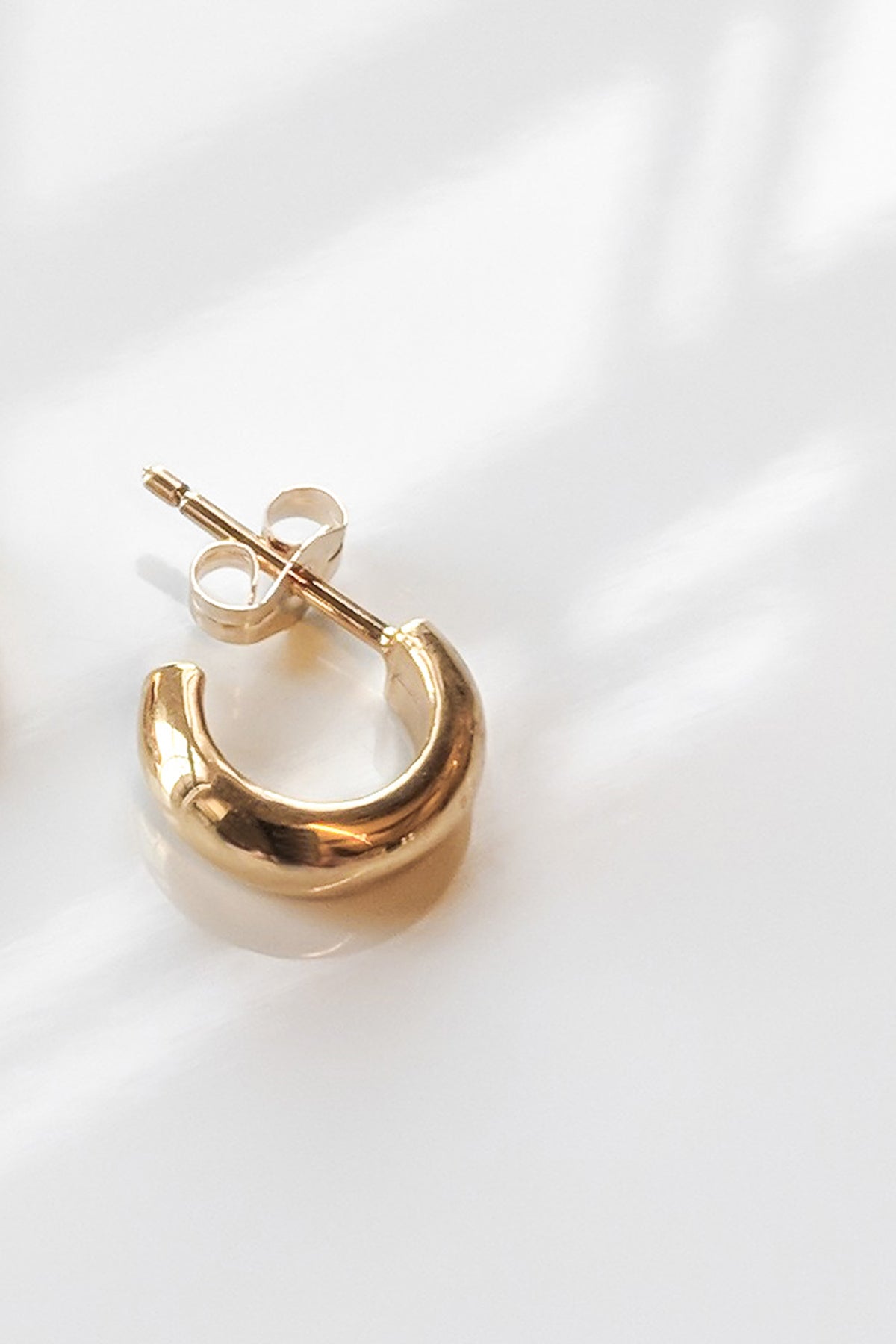 Close-up of a Thatch Vince Chunky Gold Hoop earring in 14K gold vermeil with a post and butterfly clasp, set on a white surface under soft lighting.-5730765602897