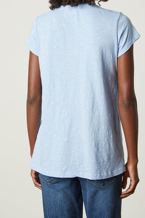 A person wearing a light blue Velvet by Graham & Spencer KIRA TEE with a scoop neckline and blue jeans, viewed from the back.