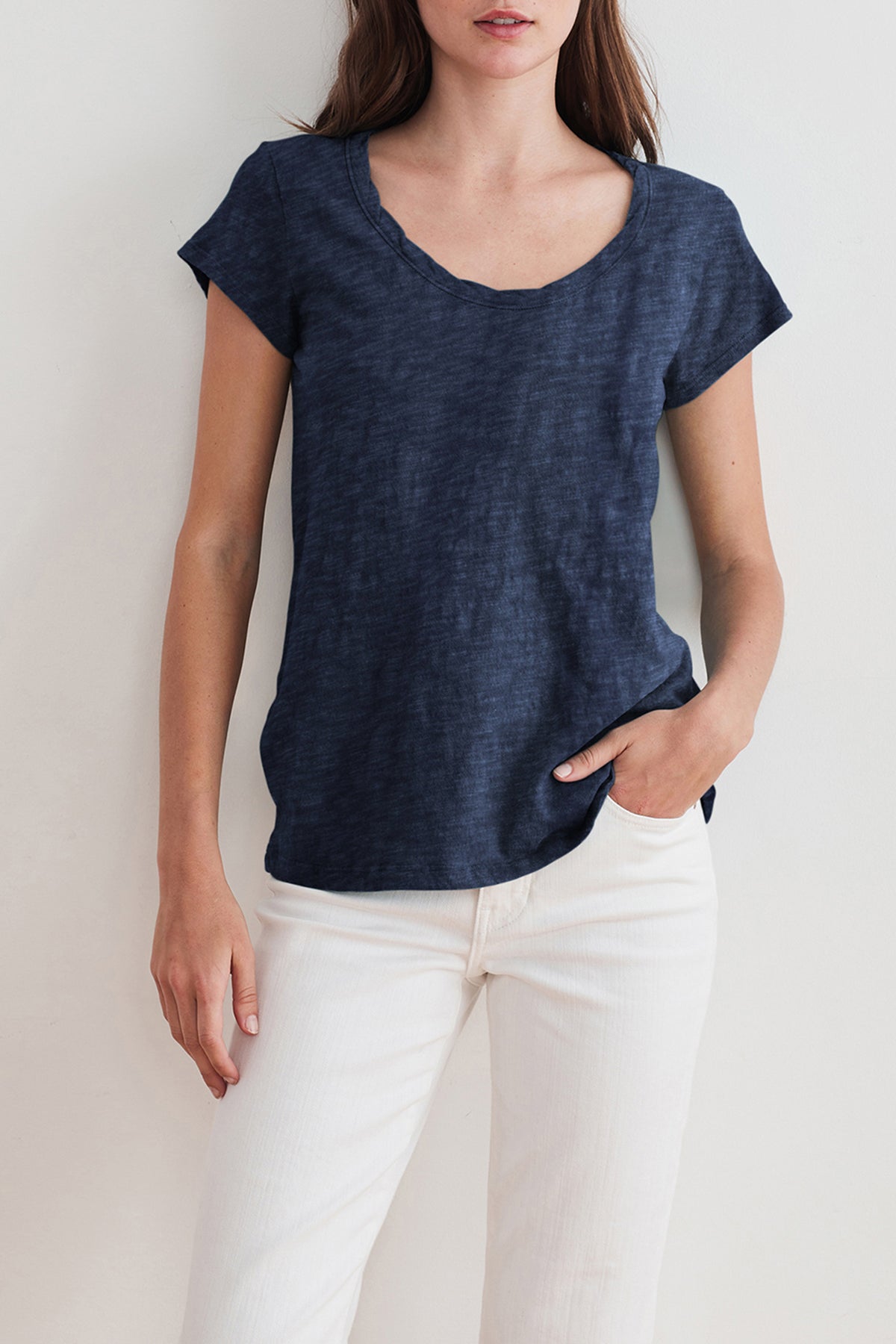 Woman wearing a navy blue KIRA TEE by Velvet by Graham & Spencer made from cotton slub fabric with a scoop neckline and white pants, with her left hand in her pocket—perfect for everyday wear.-24532839858369