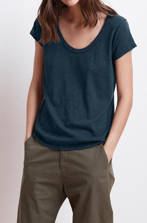 A person wearing a dark blue KIRA TEE by Velvet by Graham & Spencer and olive green pants, with hands in pockets. The face is not visible. This outfit epitomizes everyday wear with its casual yet stylish appeal.
