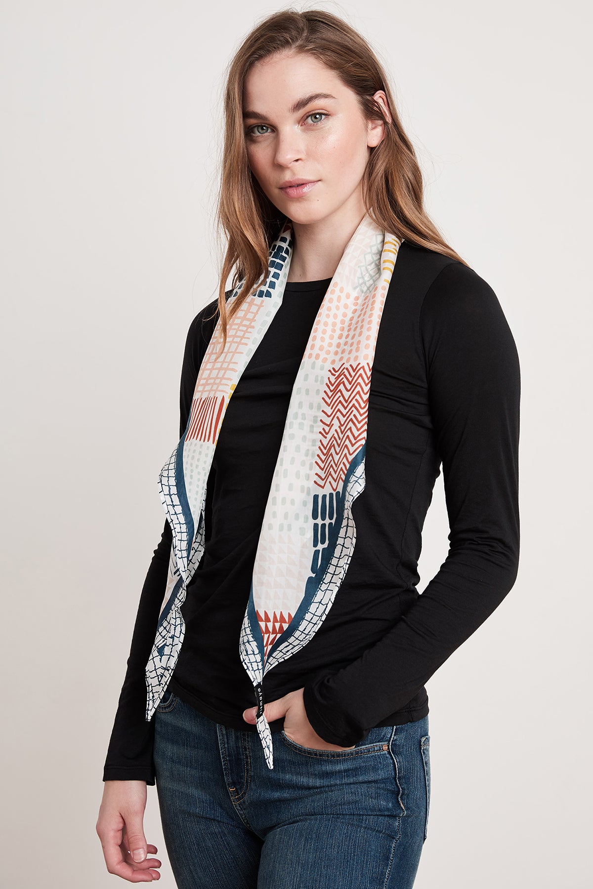 A person with long hair wearing a black long-sleeve shirt, blue jeans, and the Velvet by Graham & Spencer DIAMOND SHAPE SILK SCARF stands facing the camera against a plain background.-6705360994385