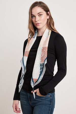 A person with long hair wearing a black long-sleeve shirt, blue jeans, and the Velvet by Graham & Spencer DIAMOND SHAPE SILK SCARF stands facing the camera against a plain background.