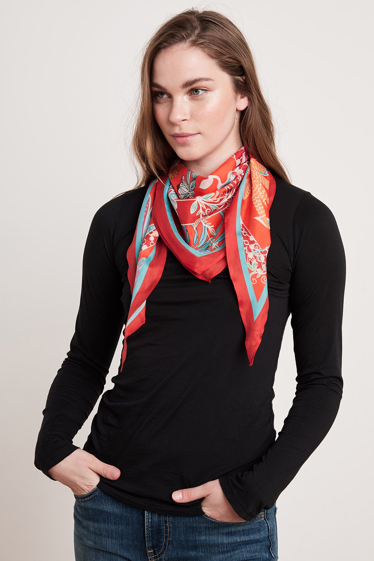 A person with a diamond silhouette and long hair wears a black long-sleeve shirt and the DIAMOND SHAPE SILK SCARF by Velvet by Graham & Spencer. They have their hands in their pockets and are looking slightly to the side.