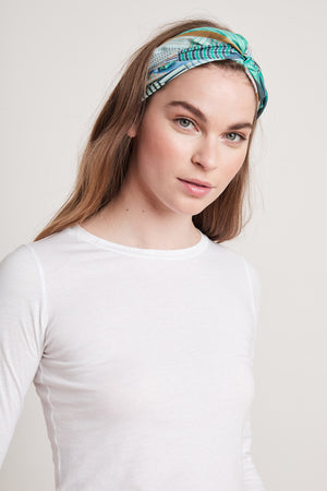 A person with long hair wearing a white long-sleeve shirt and the DIAMOND SHAPE SILK SCARF by Velvet by Graham & Spencer looks at the camera against a plain background.