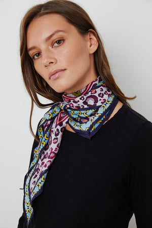 A woman with straight brown hair wearing a black shirt and a Velvet by Graham & Spencer DIAMOND SHAPE SILK SCARF loosely tied around her neck, standing against a plain white background.