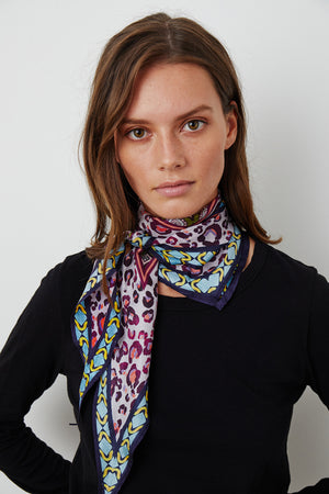 A woman in a black top wears a colorful DIAMOND SHAPE SILK SCARF by Velvet by Graham & Spencer tied around her neck.