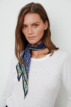 A person with long brown hair wearing a white shirt and a Velvet by Graham & Spencer DIAMOND SHAPE SILK SCARF around their neck stands against a plain background.