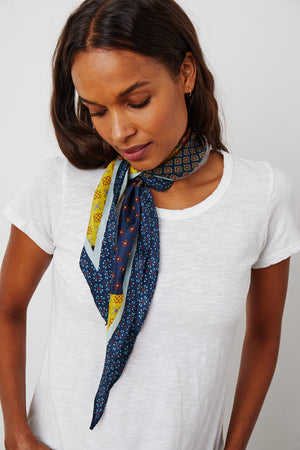 A person wearing a white t-shirt and a Velvet by Graham & Spencer DIAMOND SHAPE SILK SCARF tied around their neck looks down.