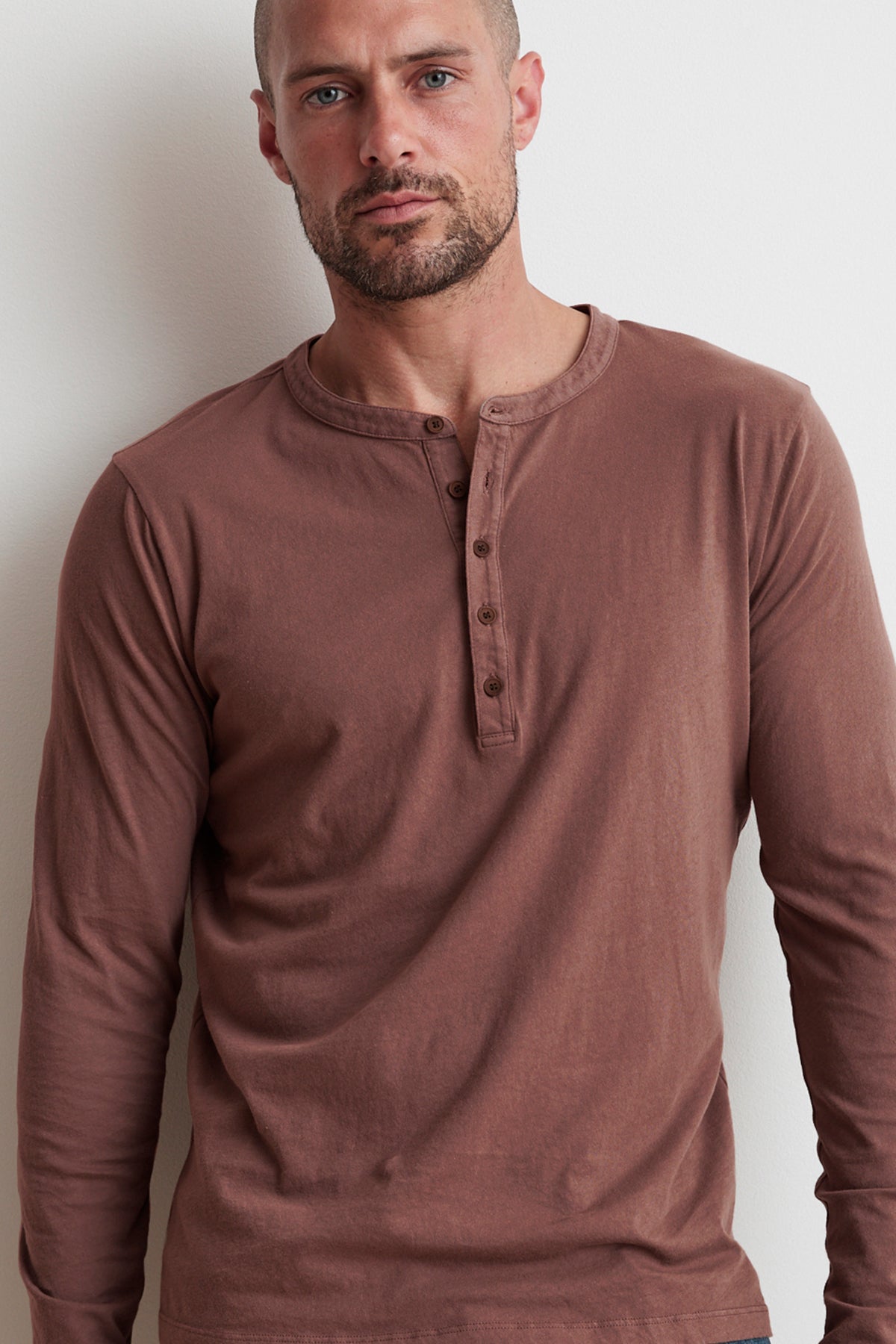 A man with a shaved head and beard wearing a Velvet by Graham & Spencer ALVARO HENLEY stands against a light-colored wall.-15914956947649