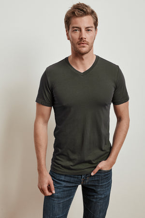 A man with short hair is wearing a dark green SAMSEN WHISPER CLASSIC V-NECK TEE by Velvet by Graham & Spencer and blue jeans, standing against a plain white background.