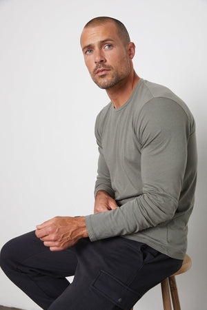 Model Sitting on Stool Wearing Skeeter Whisper Classic Crew Neck Tee in Otter