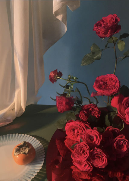 Still life of red roses beside a sheer curtain and peach on a plate