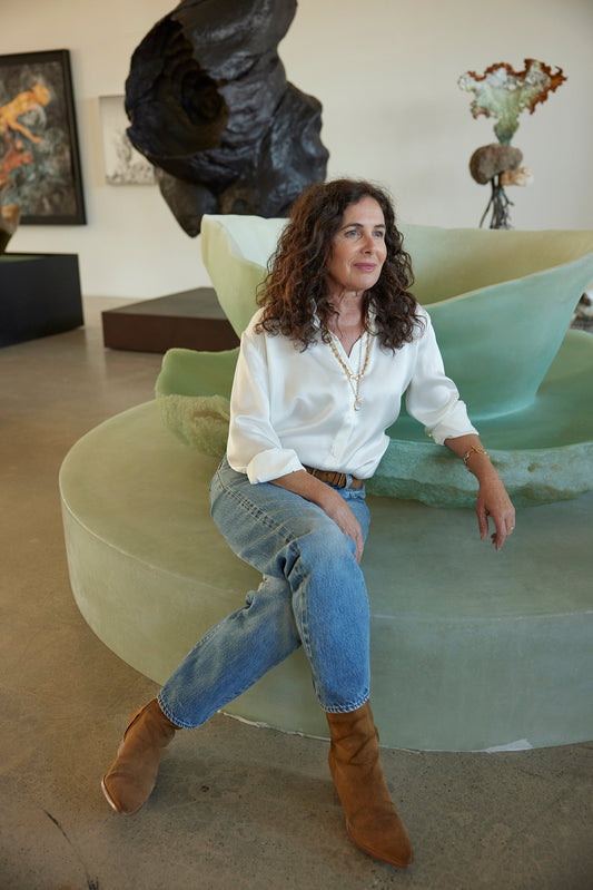 Lianne Barnes seated in a modern room wearing a white blouse and jeans beside sculptural artwork