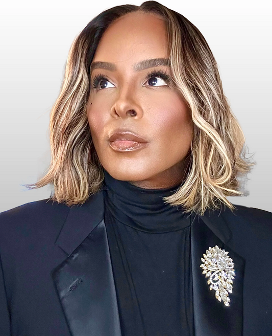Woman wearing a black blazer and jeweled brooch against a light background