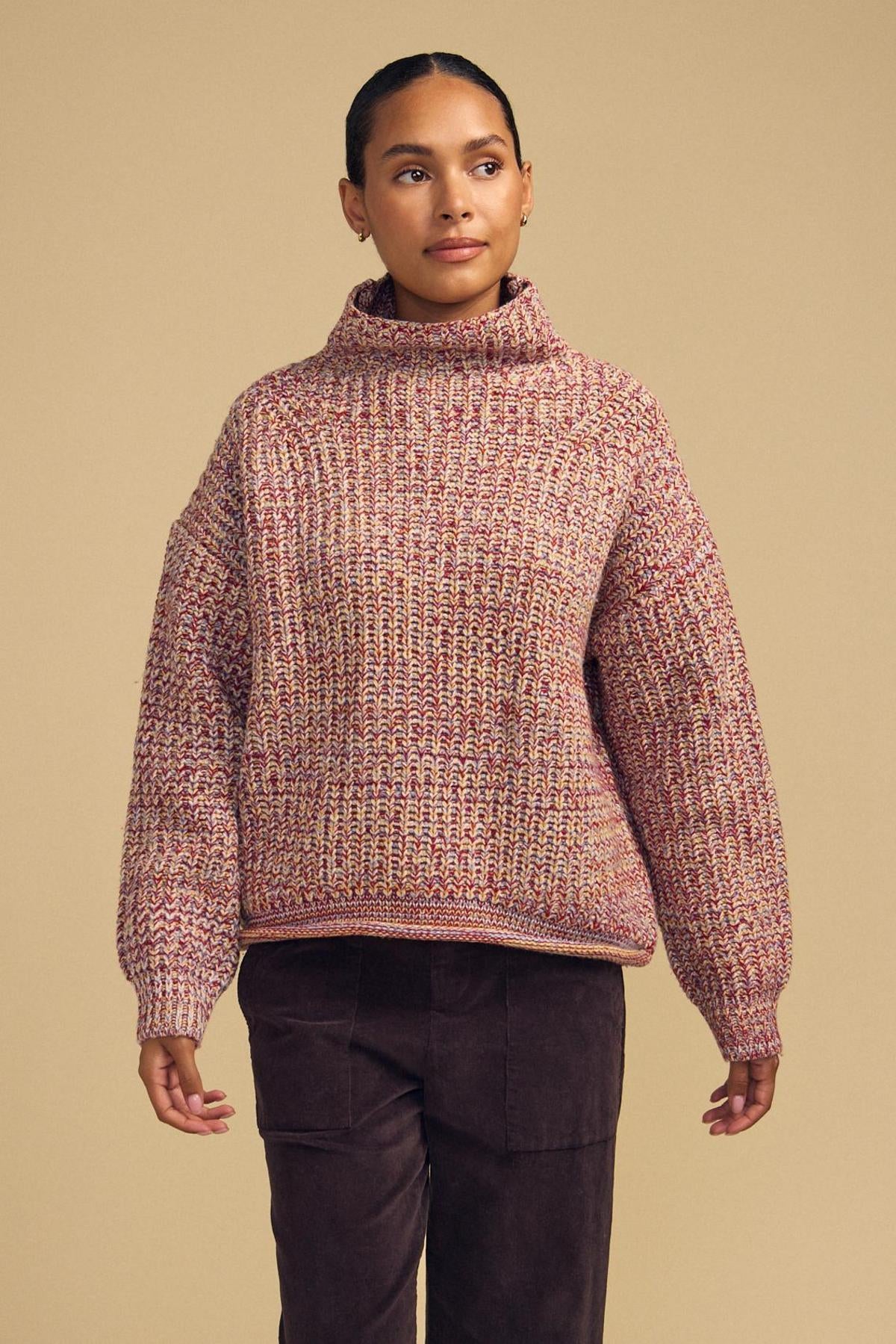Wearing the DENNIE SWEATER by Velvet by Graham & Spencer—a chunky, high-neck marled knit in shades of red and beige—paired with dark brown corduroy pants, this person stands against a plain beige background.-42181521572033