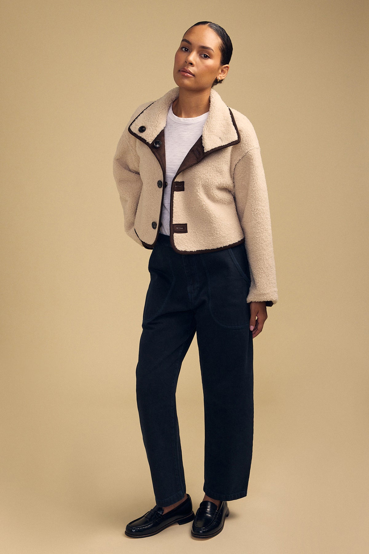 A person stands against a beige background wearing the ESME FAUX SHERPA REVERSIBLE JACKET by Velvet by Graham & Spencer, styled with a white t-shirt, navy high-waisted pants, and black loafers.-42170280280257