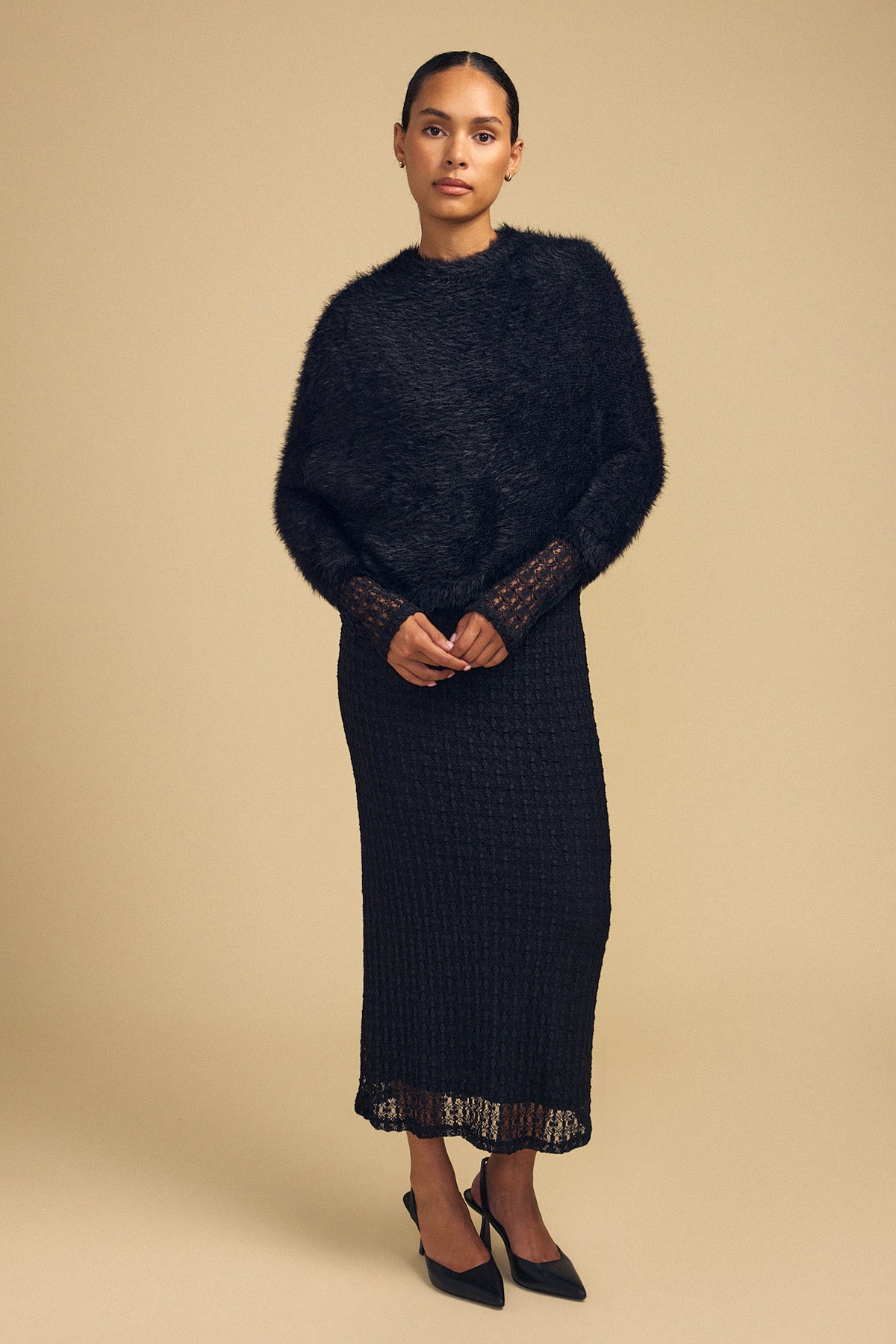 Model wearing a black LAYLA FEATHER YARN CAPE SWEATER over a matching black textured midi dress with black heels.-46488054825153