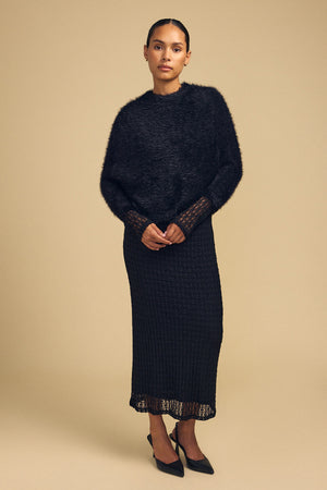 Model wearing a black LAYLA FEATHER YARN CAPE SWEATER over a matching black textured midi dress with black heels.