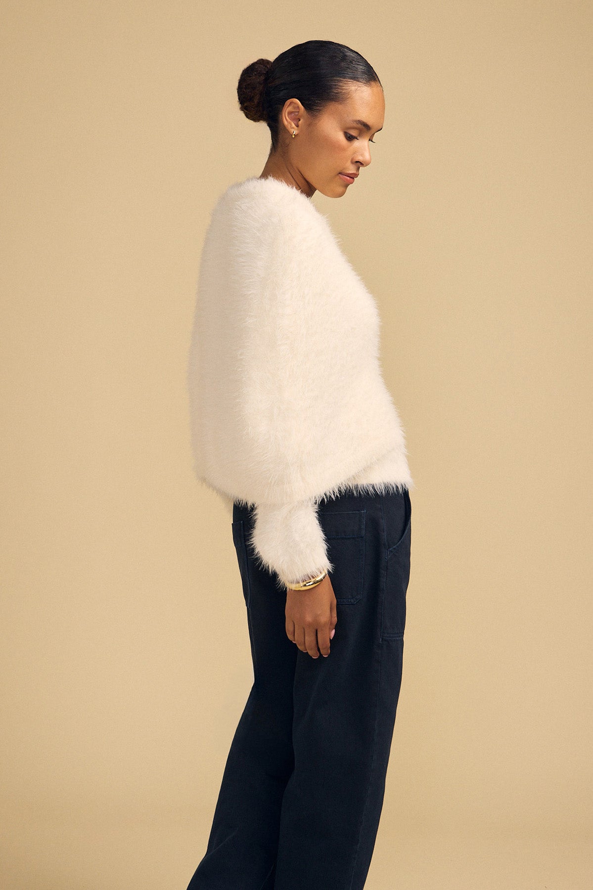 A person wearing a white, fuzzy, long-sleeved LAYLA FEATHER YARN CAPE SWEATER by Velvet by Graham & Spencer and dark trousers.-46488054464705