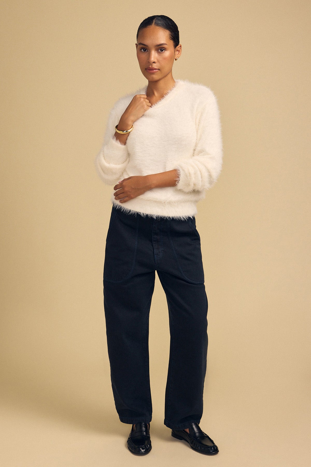 A person wears a fuzzy, cream-colored PENNY FEATHER YARN SWEATER with a V-neck, paired with dark blue wide-leg jeans and black loafers for versatile comfort.-46488052498625