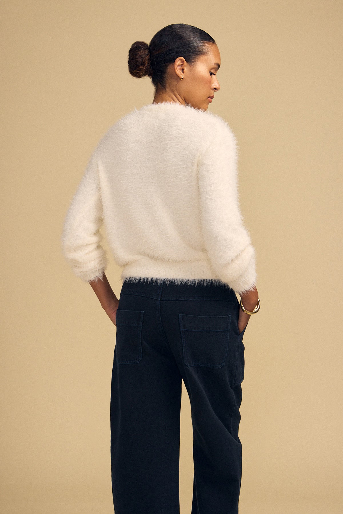 A person seen from behind wears a white fuzzy long-sleeved PENNY FEATHER YARN SWEATER by Velvet by Graham & Spencer with a classic crew neckline and dark pants, hands tucked into their pockets.