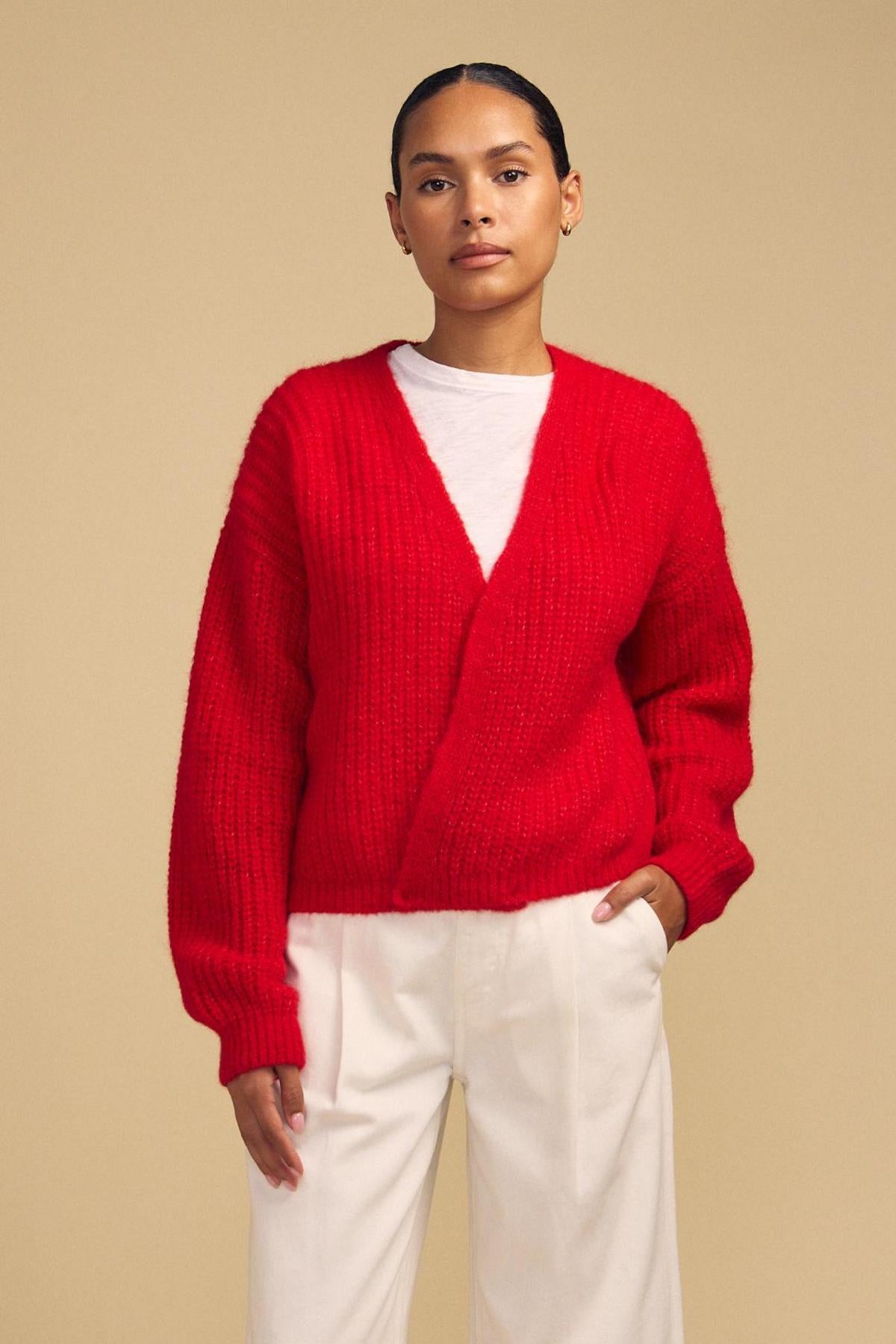 A person wearing the bright red RANYA ALPACA CARDIGAN by Velvet by Graham & Spencer, layered over a white shirt and white pants, stands against a beige background.-42181909020865