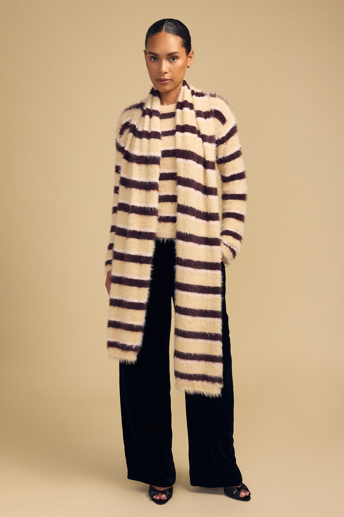 A model wears a long, fluffy SALLY FEATHER YARN STRIPED SCARF over a matching sweater and dark wide-leg trousers.-46489602162881