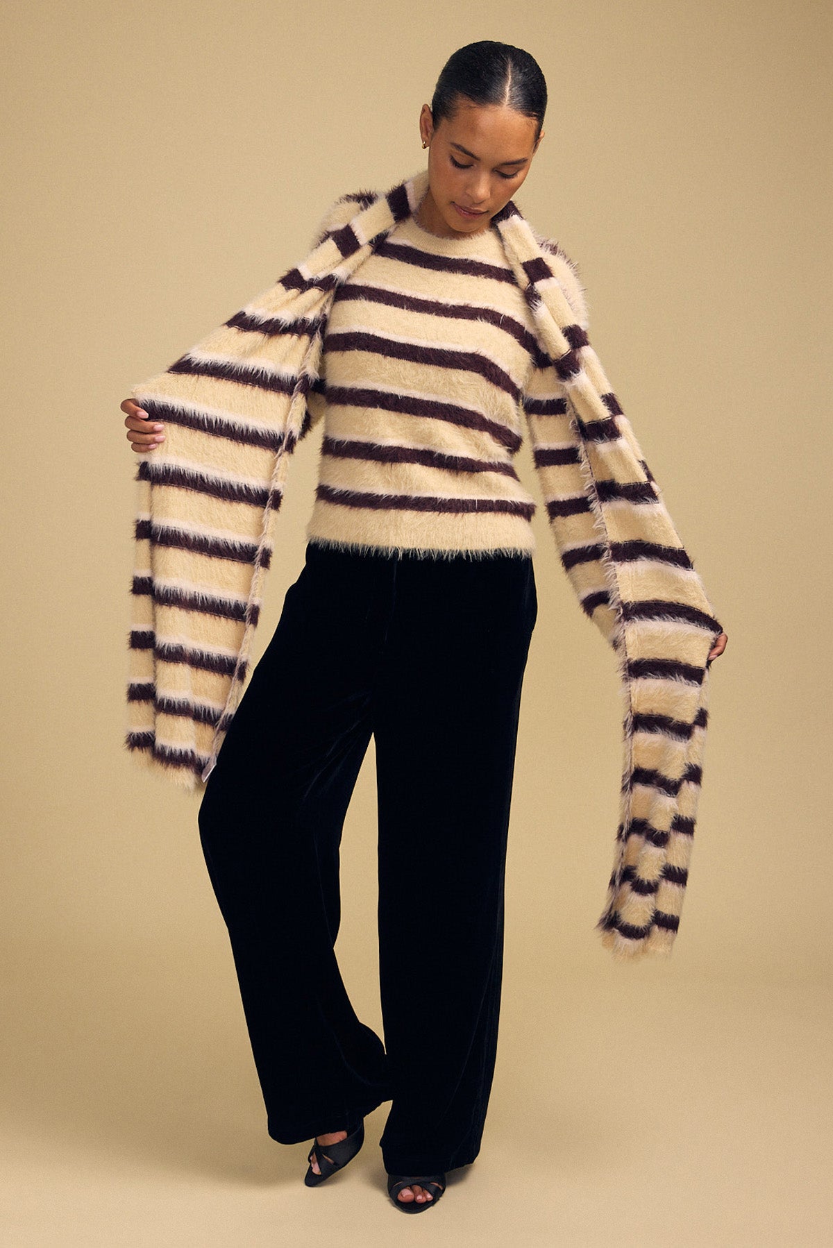 Model wearing a fuzzy, brown and cream striped sweater and matching SALLY FEATHER YARN STRIPED SCARF, paired with black wide-leg trousers.