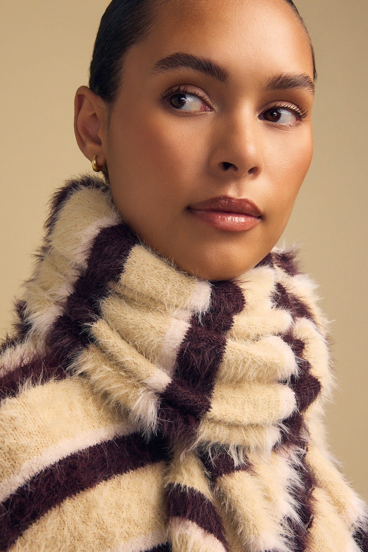 Close-up of a person wearing a cozy, striped cream and dark brown SALLY FEATHER YARN STRIPED SCARF.-46489602261185