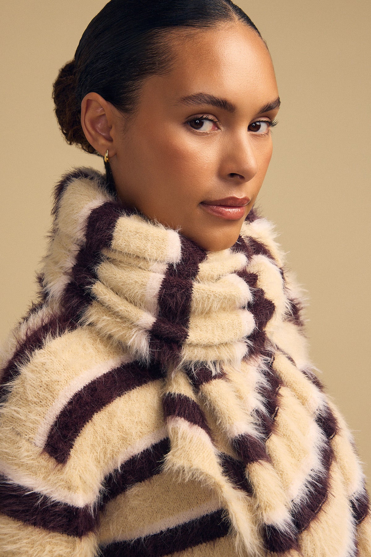 A person wearing a cozy, thick-knit SALLY FEATHER YARN STRIPED SCARF featuring wide cream and dark brown bands.