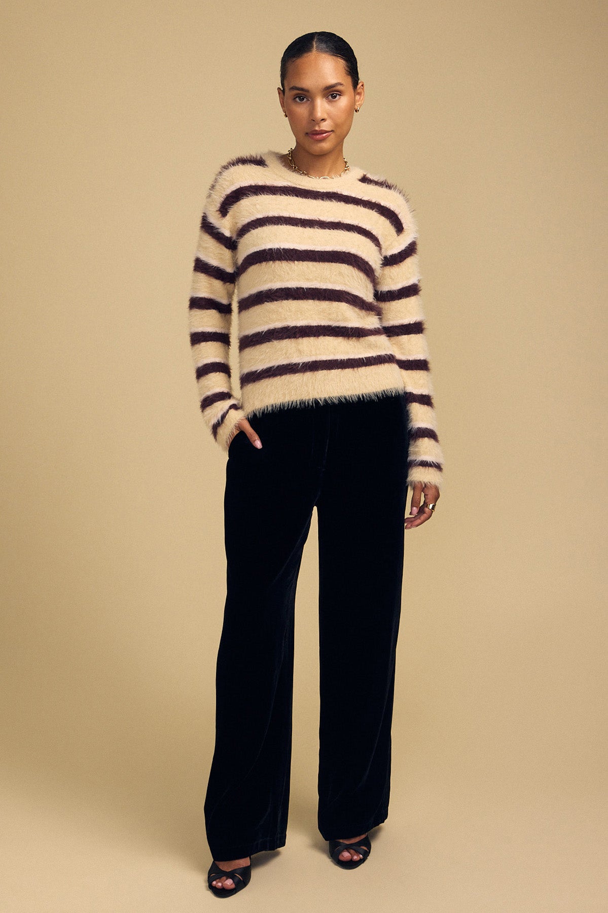 A person wearing a cozy, cream and brown striped TINA FEATHER YARN SWEATER by Velvet by Graham & Spencer paired with black wide-leg trousers.-46489738510529