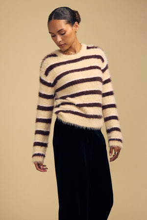 A person wearing a cozy, cream and dark brown striped TINA FEATHER YARN SWEATER by Velvet by Graham & Spencer with dark trousers.