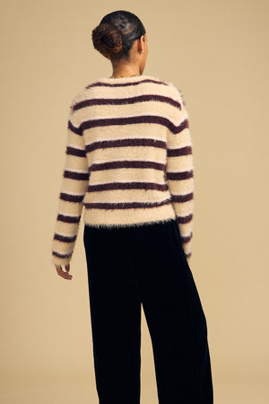Back view of a person wearing a TINA FEATHER YARN SWEATER in a cozy, cream and dark brown striped crew neck design with black trousers.