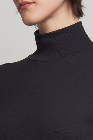 Close-up of a person wearing the AGOURA DRESS by Velvet by Jenny Graham, featuring a fitted silhouette and ribbed cotton black turtleneck design, highlighting their chin and neck.