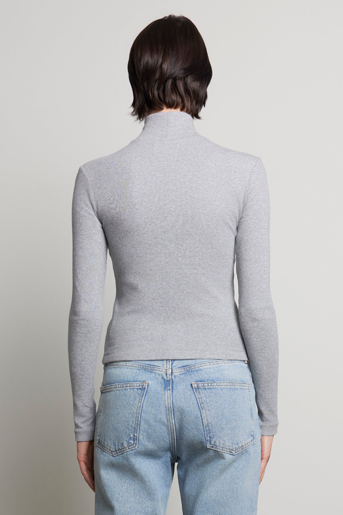 A person with short brown hair is wearing the HELMS TEE by Velvet by Jenny Graham in gray with a ribbed texture turtleneck and paired with light blue jeans, shown from the back.-38318596817089