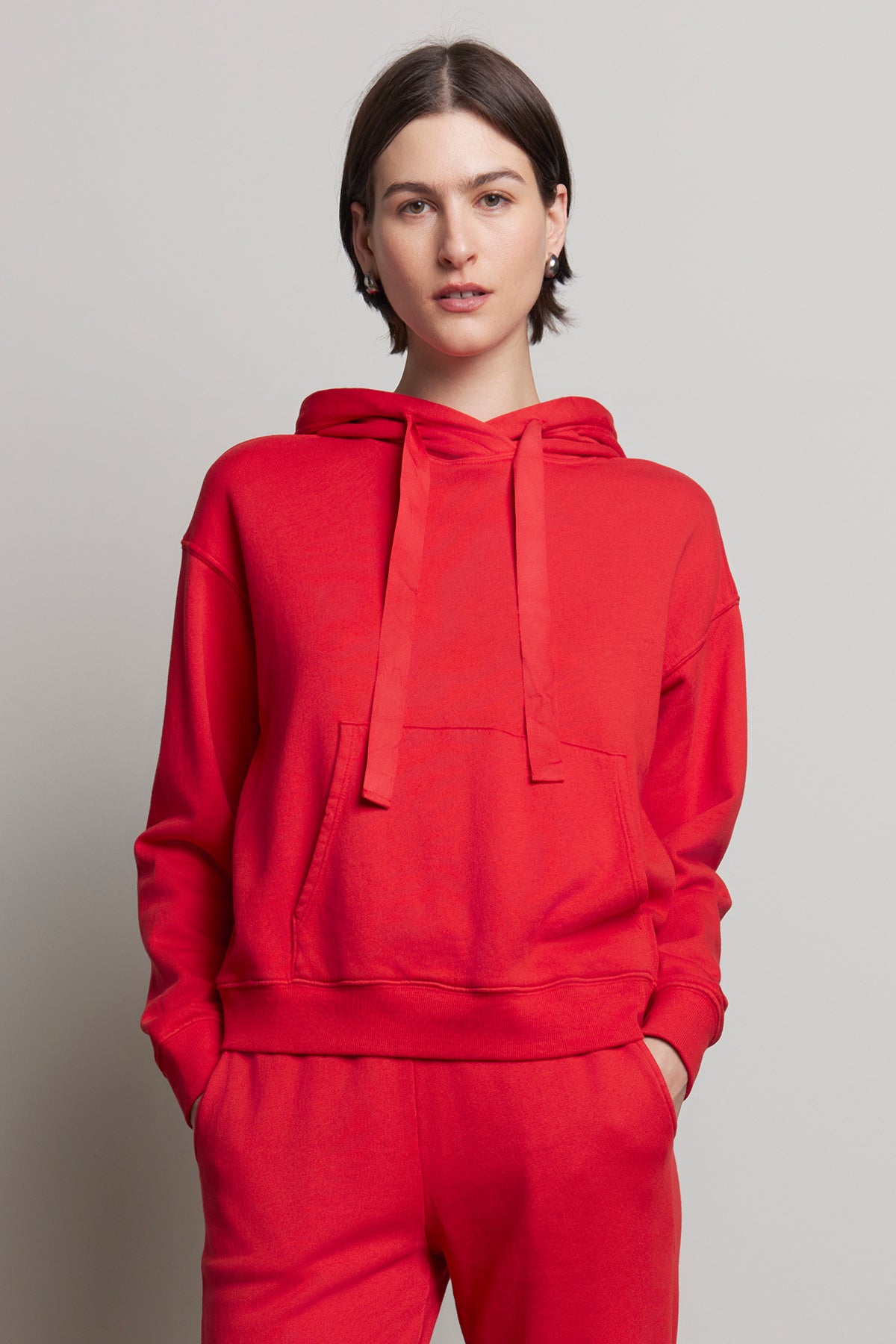 A person wearing an OJAI HOODIE from Velvet by Jenny Graham, made of organic cotton in red, along with matching pants, stands against a plain background.-38318612512961